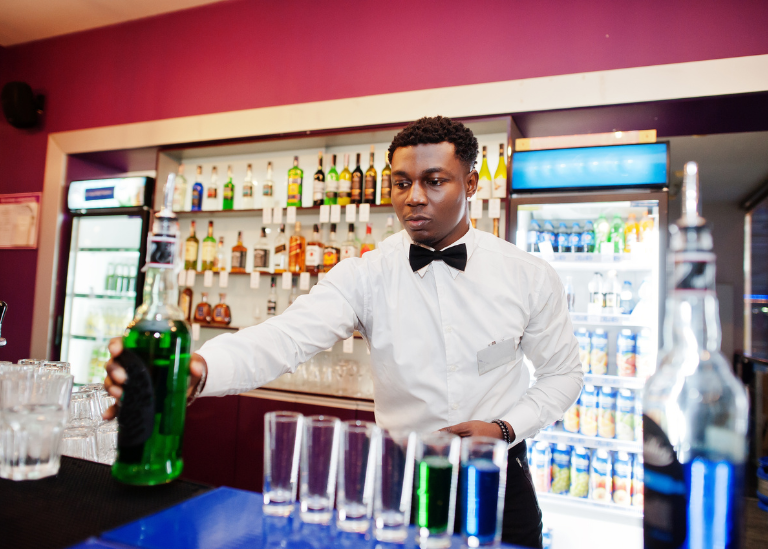 Bartender pouring green liquor into shot glasses at a vibrant bar setting, highlighting Tennessee's liquor liability context.