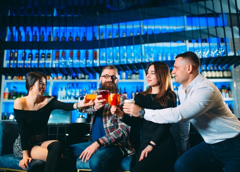 Group of friends toasting with colorful cocktails in a bar setting, highlighting social interaction and nightlife, relevant to Kentucky dram shop law discussions.