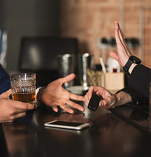 Two individuals engaged in a discussion at a bar, one holding a glass of whiskey, emphasizing communication and interaction related to dram shop consulting and legal insights.