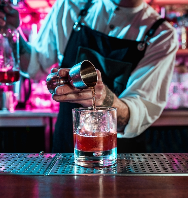 Bartender pouring a cocktail into a glass with ice, highlighting alcohol service in a bar setting related to dram shop liability.