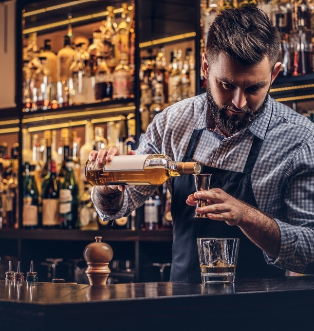 Bartender pouring whiskey into a glass, illustrating alcohol service in a bar setting relevant to dram shop law discussions.